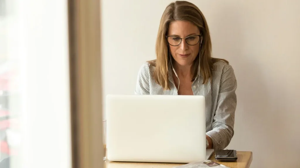 Woman sitting down near table in front of white laptop reading about pay transparency