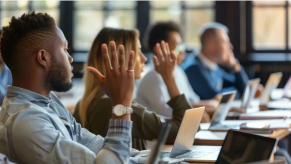 Employees in a training session raising their hands to participate, with laptops open, illustrating a culture of continuous learning in the workplace.